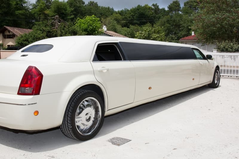 A Chrysler limo parked in a park with tainted glasses and green trees in the background